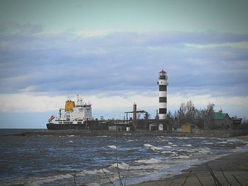 Lighthouse on beach against cloudy sky