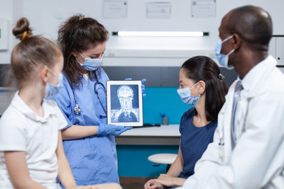 Nurse wearing mask showing digital tablet in clinic