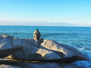 Rear view of person sitting on rock in sea against sky