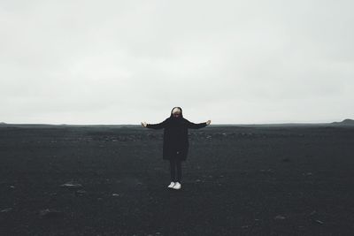 Woman with arms outstretched standing on sand at black beach