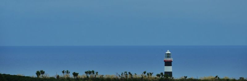 Lighthouse by sea against clear sky