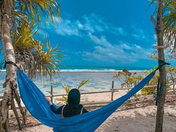 Man relaxing on hammock at beach against sky