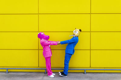 Full length of a man holding yellow umbrella against wall