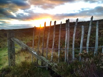 Fence on field against cloudy sky