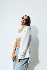 Young woman wearing sunglasses while standing against white background
