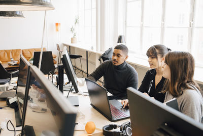 High angle view of it professionals discussing over laptop on desk in office