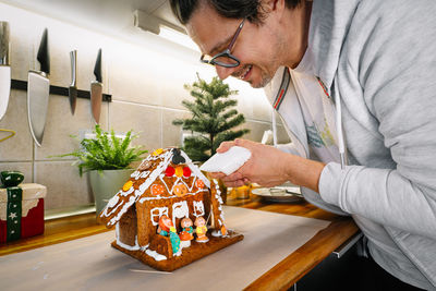 Man preparing gingerbread house in kitchen at home