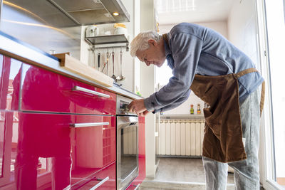 Senior man with apron preparing food in oven at kitchen