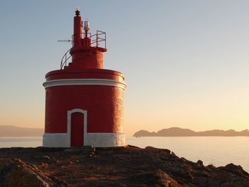 Lighthouse by sea against clear sky during sunset