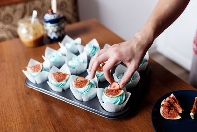 Decorating homemade chocolate muffins with blue cream topping and fig
