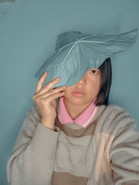 Portrait of woman holding leaf on head against blue background