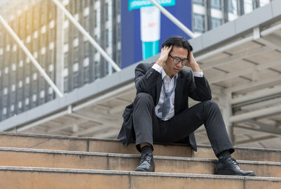 Businessman with headache sitting on staircase against office building