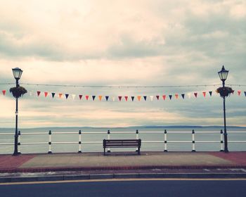 Empty bench at seashore against cloudy sky