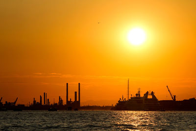 Silhouette ship in sea against orange sky
