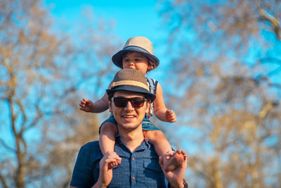 Portrait of father carrying daughter on shoulders against bare trees