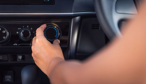 Cropped hand of woman adjusting air conditioner button in car