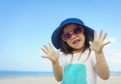 Portrait of young girl wearing sunglasses and hat against clear blue sky