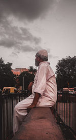 Rear view of man sitting on rock against sky