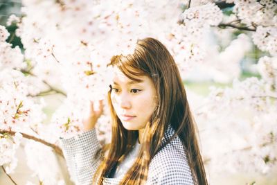 Thoughtful young woman by flowering tree at park