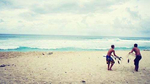 Rear view of men on beach against sky