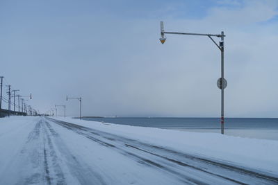 Arrow signs on pole over snow covered road against sky