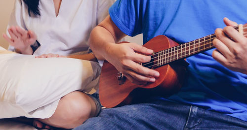 Midsection of man playing ukulele while sitting with female friend on seat