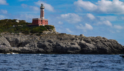 Lighthouse by sea against buildings