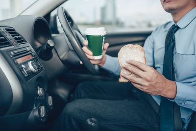 Midsection of man holding coffee while sitting in car