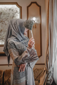 Midsection of woman holding window at home with hijab fashion