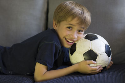 Portrait of boy with soccer ball lying on sofa at home