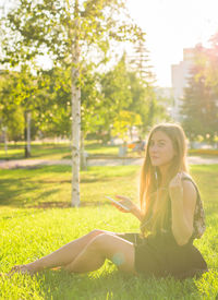 Young woman sitting on field against trees