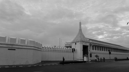 People in front of building against cloudy sky