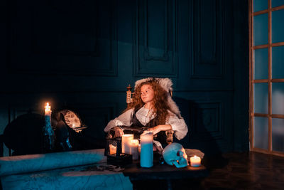 Young woman sitting on table against illuminated wall