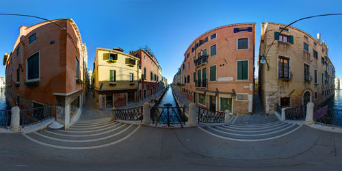 Fish-eye view of canal amidst buildings in city against clear sky