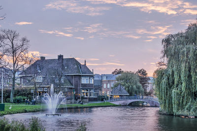 Buildings by lake against sky during sunset