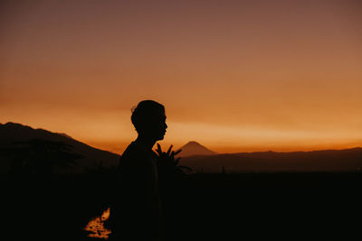 Silhouette person standing on land against sky during sunset