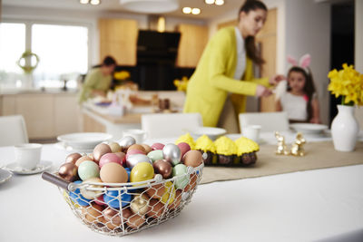 Easter eggs in basket on table at home with mother and daughter in background