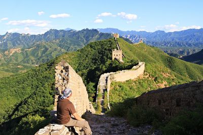 Rear view of man sitting on retaining wall at mountain