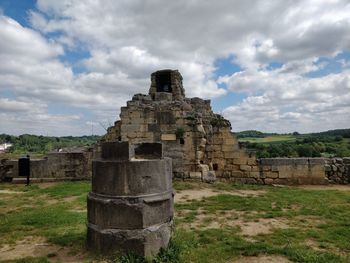 Old ruins on field against cloudy sky