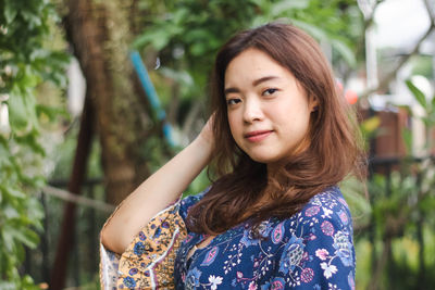 Portrait of young woman standing against trees