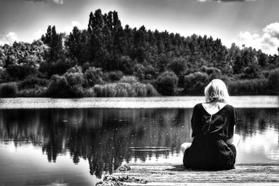 Woman sitting by lake against sky