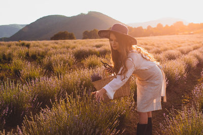 Rear view of woman with umbrella on field against sky during sunset