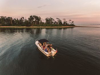 People sitting on boat sailing in river against sky at sunset