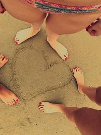Low section of friends standing by heart shape at beach