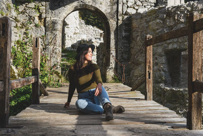 Young woman sitting on footbridge of old castle ruin, autumn, fall, earth tones, style.