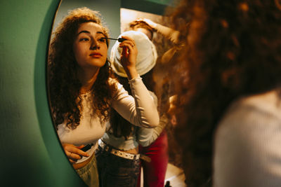 Young woman applying mascara while looking in mirror