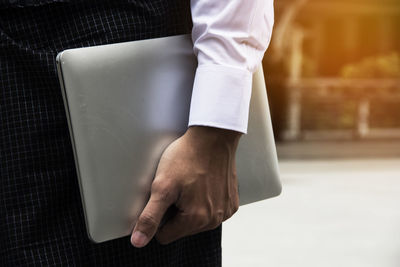 Midsection of businessman holding laptop while standing outdoors