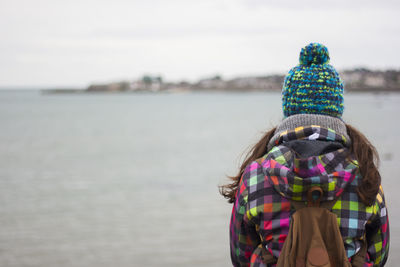 Rear view of young woman standing by sea