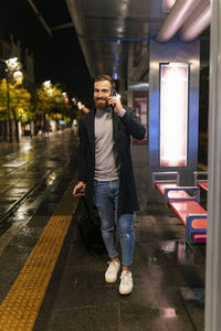 Smiling man holding suitcase and talking on mobile phone at tram station