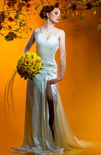 Beautiful bride holding bouquet while posing against orange background